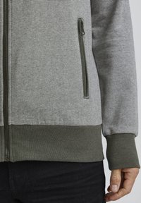 Grijze en witte gestreepte zip-up jacket met groene geribbelde manchetten en onderkant, met een zijzak en een gestructureerde stof.