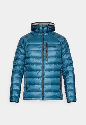 Giacca a vento blu con cappuccio, caratterizzata da una chiusura lampo frontale, accenti neri, motivo trapuntato e logo Columbia Titanium sul petto.