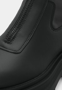 Mustad pahkluu saabaste eesmine tõmblukuga mudel, sileda nahapinnaga, ümarate varvastega ja paksu, vastupidava tallaga.