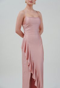 Rosa satin kjole med tynne stropper, med rynket sideløsning og høyt splitt. Glatt tekstur med en tettsittende silhuett.