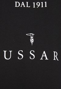 Camiseta negra con texto blanco: "DAL 1911" encima de un logo gráfico, con "USSAR" debajo. Tela de algodón suave. Elementos de diseño simples.