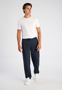 Donkerblauwe joggingbroek met een elastische tailleband en een trekkoord, gecombineerd met een aansluitend wit T-shirt met korte mouwen en witte sneakers.