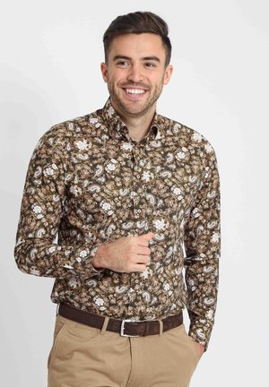 Bruine overhemdd met paisleypatroon, voorzien van een button-down kraag, lange mouwen en witte florale accenten, gedragen met beige chinos en een bruine riem.