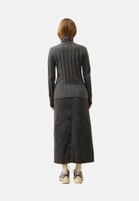 Szary prążkowany sweter typu golf z dopasowanym krojem, połączony z długą czarną spódnicą dżinsową, białymi skarpetkami i masywnymi trampkami.