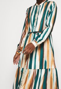 Abito lungo con bottoni in un tessuto setoso, caratterizzato da strisce verticali in teal, marrone e crema. Include una cintura in tessuto e maniche arricciate.