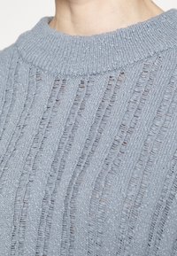 Maglione lavorato a maglia di un blu chiaro, con un motivo testurizzato che presenta linee verticali e un ampio colletto a costine. Tessuto morbido e leggero.