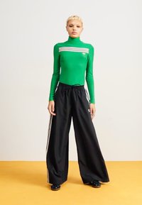 Camisola verde de manga longa com riscas horizontais, combinada com calças largas pretas com riscas brancas laterais. Tecido suave, ajuste descontraído.