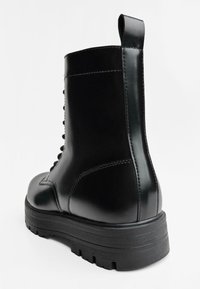 Stivaletto in pelle nera con finitura testurizzata, punta rotonda e suola in gomma spessa. Presenta un tassello per una facile calzata e una chiusura con lacci.