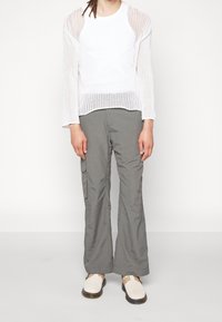 Suéter blanco de punto con un motivo de estrella, combinado con pantalones cargo grises con bolsillos laterales. El calzado consiste en zapatos sin cordones de color claro.
