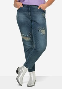 Vaqueros desgastados en azul con rasgaduras y cuentas decorativas en varios colores. Corte recto con bolsillos y una cintura de altura media.