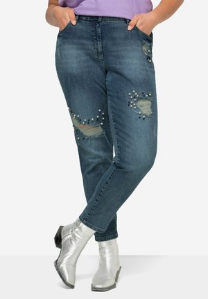 Vaqueros desgastados en azul con rasgaduras y cuentas decorativas en varios colores. Corte recto con bolsillos y una cintura de altura media.