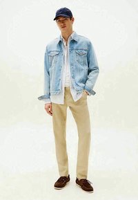 Jeansjacka i ljusblått, lagrad över en vit skjorta och beige byxor. Marinblå keps, bruna seglarskor och en avslappnad passform fulländar stilen.