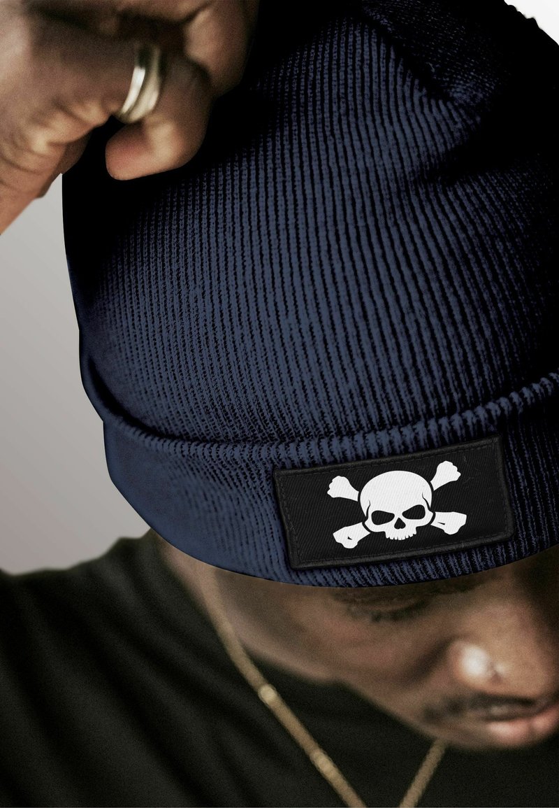 Navy knit beanie with ribbed texture, featuring a black patch with a white skull and crossbones design.