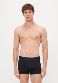 Schwarze Boxershorts mit einem breiten, dunkelblauen Bund, auf dem "HILFIGER" in erhabenen Buchstaben steht. Der Stoff wirkt glatt und anliegend.