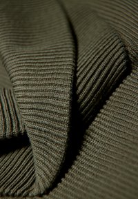 Rippstoff aus olivgrünem Baumwollstrick mit einer weichen Textur, der überlappende Schichten und feine Nähte zeigt.