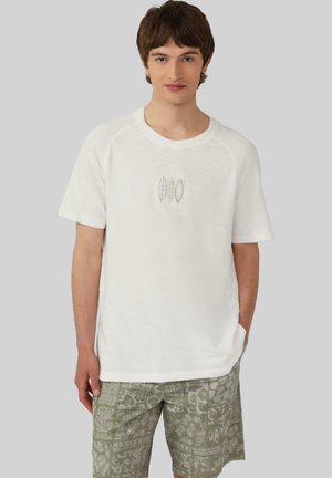 T-shirt blanc à manches courtes avec col rond et col côtelé, présentant des motifs imprimés discrets de couleur gris clair. Accompagné d'un short vert à motifs.