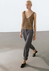 Brown lace top with a deep V-neck and ruffled hem, paired with gray tapered pants and black slip-on shoes. Minimalist design, textured fabric.