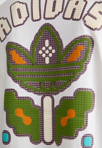 Hvid t-shirt i stof med et tekstureret grafisk design af en grøn, brun og orange blomst med "Adidas" i fede, flerfarvede bogstaver.