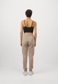 Sort cropped tanktop og lysebrune sweatpants med elastisk talje, set fra ryggen. Sneakers er synlige forneden.