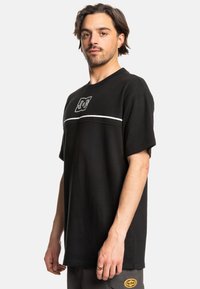 Black textured crewneck t-shirt featuring a white stripe across the chest and a logo graphic. Short sleeves and relaxed fit.