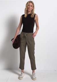 Bruine mouwloze top, grijze joggerbroek met trekkoord en zijzakken, gecombineerd met witte sneakers en een bruine schoudertas.