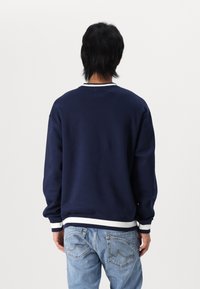 Granatowa bluza z białym prążkowanym kołnierzem i mankietami, charakteryzująca się luźnym krojem i klasycznym wzorem. Noszona z jasno-niebieskimi dżinsami.