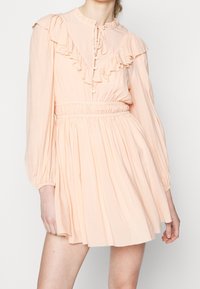 Vaate vaaleanpunaista persikkaa, jossa on rypytetty kaula-aukko ja hihat, joustava vyötärö ja avara hameosa. Kevyttä kangasta, jossa on napit. 