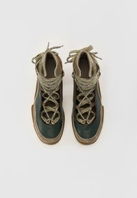 Lace-up shoes made of dark green leather with olive textile accents and a brown suede heel, featuring a textured design and round laces.