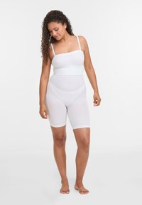 Lenjerie modelatoare albă, cu un top fără mâneci și pantaloni scurți până la mijlocul coapsei, realizată dintr-un material neted și elastic, cu un design fără cusături.