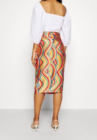 Jupe midi colorée avec un motif ondulé en rose, bleu, jaune et vert. Fabriquée en tissu lisse, elle a une silhouette ajustée et une fente sur le côté.