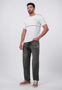 Hvit T-skjorte med svarte horisontale detaljer, sammen med mørkegrå jeans og brune joggesko, som viser en avslappet passform og klassisk design.