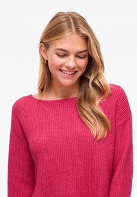 Pull moulant rose tricoté avec texture côtelée, encolure large et manches longues, présentant une apparence douce et confortable.