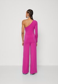Fuchsia jumpsuit med én lang erm og et eksponert skulder. Flared bukser skaper en flytende silhuett. Har skinnende, metalliske hæler.