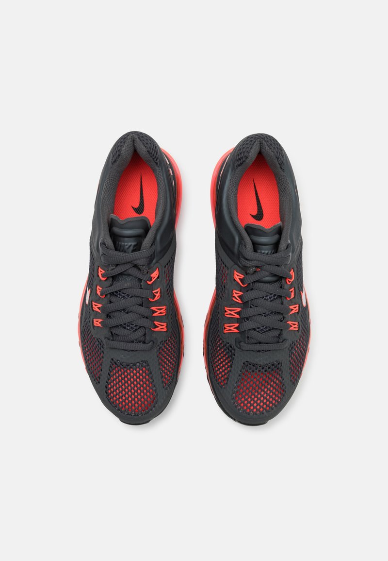 Zapatillas deportivas negras y rojo brillante con parte superior de malla, punta redonda, cordones planos y marca visible. Suela texturizada y detalles de ventilación.