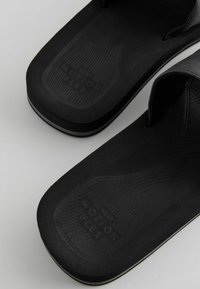 Schwarze Flip-Flops mit einer strukturierten Fußbett und glatten Riemen, mit "MOTION FLEX" auf der Sohle eingestanzt, und einer weißen Akzentschicht.