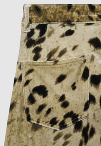 Beiger Stoff mit schwarzen unregelmäßigen Flecken, die ein Leopardenmuster bilden, mit gesticktem Gesäßtaschen- und Gürtelschlaufe-Detail.