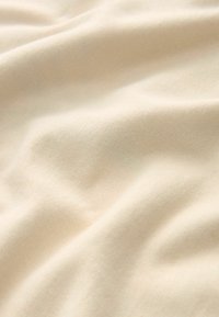 Beżowa bawełniana tkanina o miękkiej fakturze, z delikatnymi zmarszczkami i gładką powierzchnią. Idealna do odzieży lub tkanin domowych.