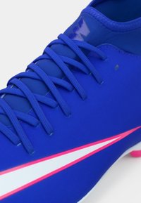 Μπλε ποδοσφαιρικό παπούτσι με λείο συνθετικό άνω μέρος, με περίπλοκο δέσιμο, λευκή και ροζ ρίγα, και επενδυμένο γιακά στο άνοιγμα.