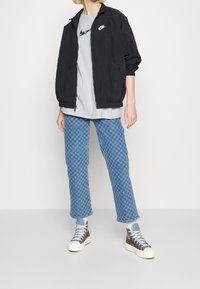 Černá lehká zipová bunda, šedé tričko, modré kostkované kalhoty a hnědé vysoké tenisky s bílou podrážkou. Neformální, moderní outfit.