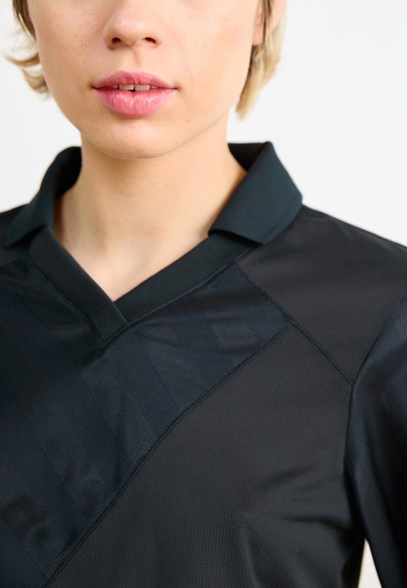 Polo nero con colletto strutturato e tessuto testurizzato caratterizzato da un motivo diagonale. I dettagli delle cuciture sono visibili nella zona delle spalle.