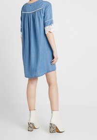 Džínové šaty s kulatým výstřihem a krátkými rukávy. Mají krajkový lem na rukávech. Oblečeny s bílými kotníkovými botami a sandály s hadím potiskem.