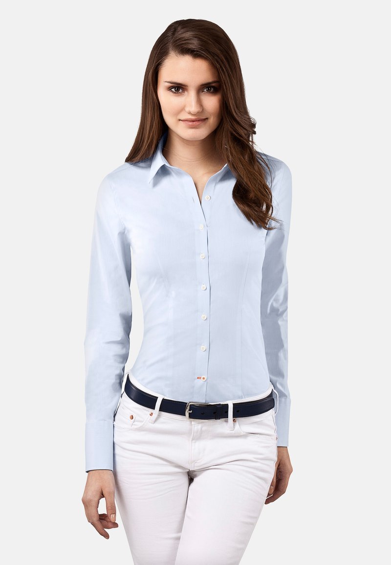 Chemise bleu clair à boutons avec des manches longues, au design ajusté et à la texture lisse, associée à un pantalon blanc et une ceinture bleu foncé.