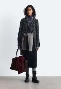 Black floral-patterned shirt over a checkered turtleneck, grey sweater tied at the waist, black pencil skirt, and chunky black boots. Brown handbag with red scarf.