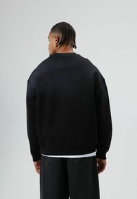 Zwarte sweatshirt met een losse pasvorm en verlaagde schouders, voorzien van geribbelde manchetten en zoom, gecombineerd met losse zwarte broek.