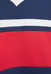 Sveter z bavlnenej zmesi s výstrihom do V a horizontálnymi pruhmi v námorníckej modrej, bielej a červenej farbe. Hladká textúra s kontrastnými farebnými blokmi.
