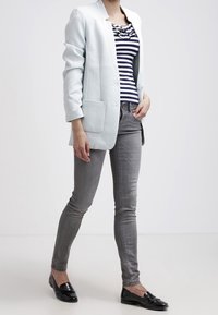 Hellblaues Blazer über einem schwarz-weiß gestreiften Oberteil, kombiniert mit grauen Slim-Fit-Jeans und schwarzen Mokassins. Glatter Stoff, l�ässiges Design.