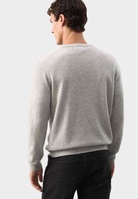 Jasnoszary sweter z miękkiego materiału, okrągły dekolt, ściągacze na rękawach i u dołu, noszony na czarnych spodniach, pokazany z tyłu.