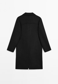 Czarny wełniany płaszcz o długim, prostym kroju, z wklęsłym kołnierzem i długimi rękawami. Posiada centralny szew i rozcięcie z tyłu.