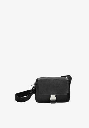 Črn pravokoten crossbody nahrbtnik z sprednjim pokrovom, srebrnim kovinskim zaponko, zadrgo in nastavljivim tekstilnim trakom na bele podlagi.
