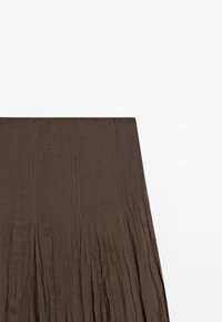 Mørkebrun plisseret nederdel med høj talje, lavet af letvægts tekstureret stof, vist fladt mod en hvid baggrund.